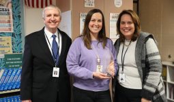 Three people posing with a trophy in front of a classroom setting.